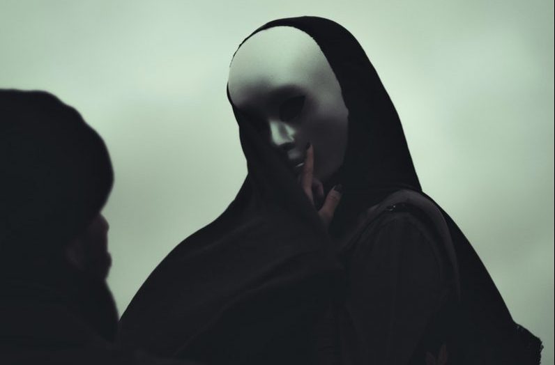 Black and white of anonymous man and anonymous person in white mask touching covered face